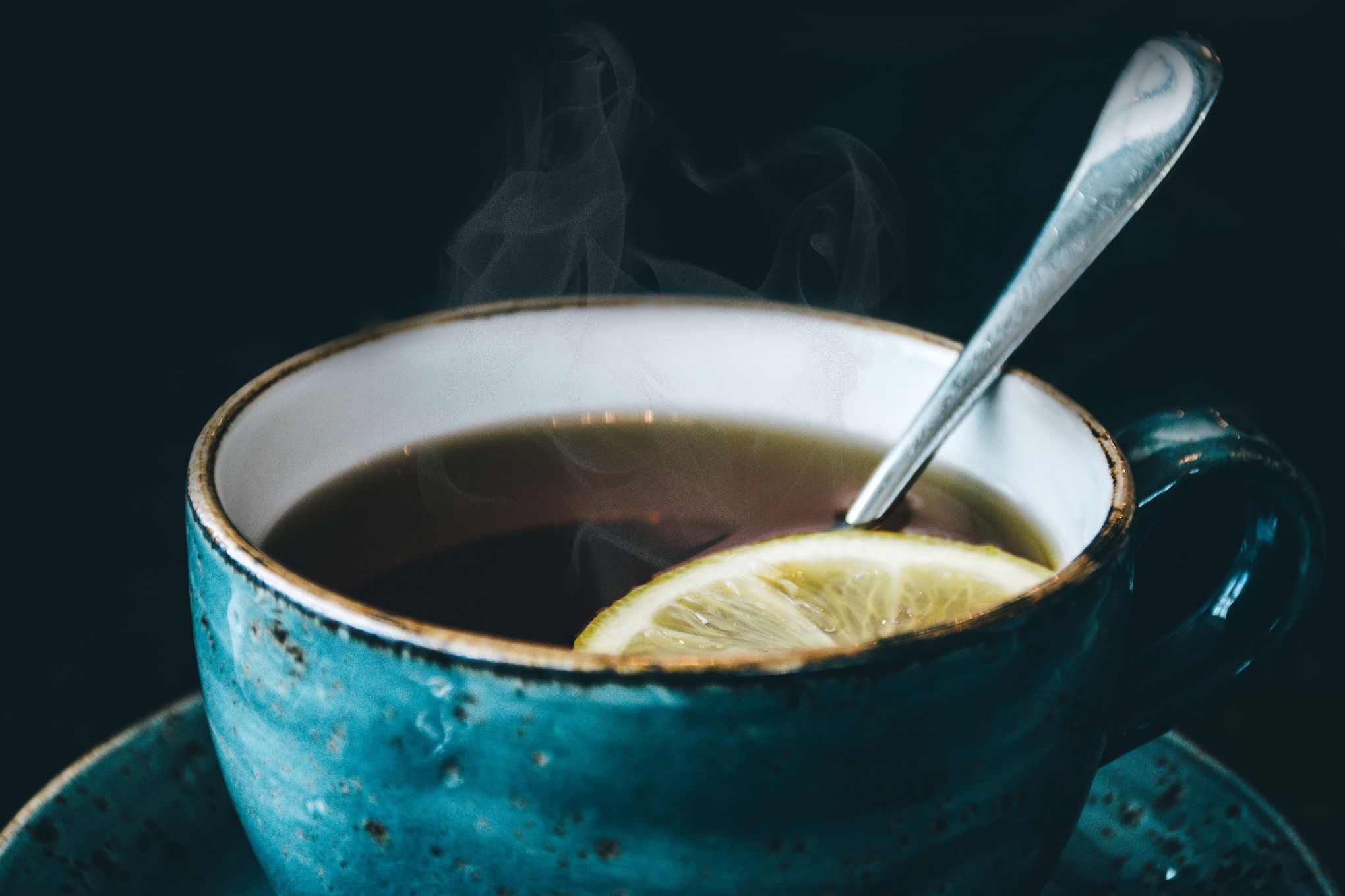 Picture of a blue tea cup with tea inside of it as well as a slice of lemon and a teaspoon