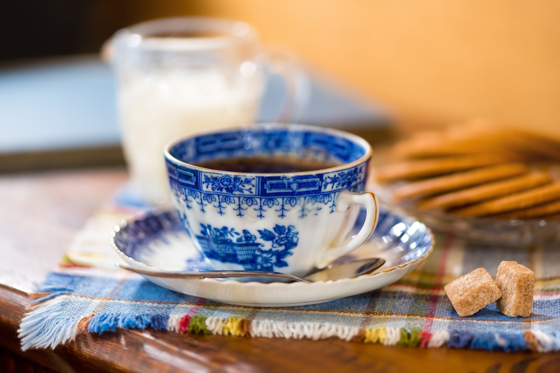 Picture presenting a blue and white cup of tea on a table with food and milk jar in the background