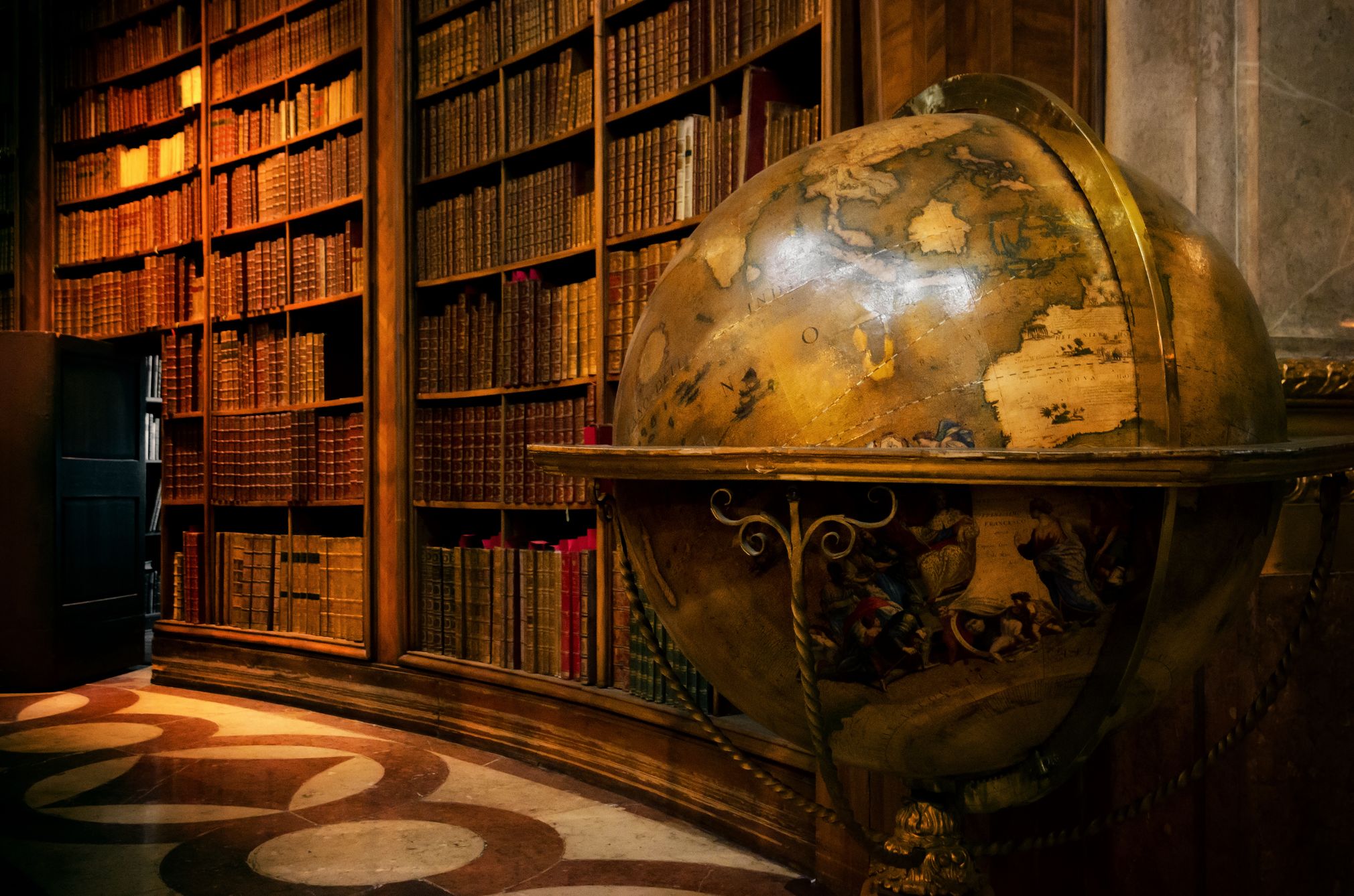 Image of the library with many books on the background and an antique earth globe in the foreground